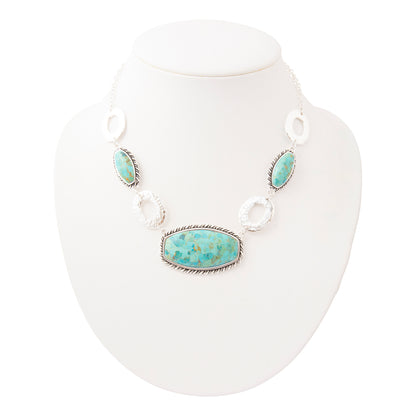 A silver-toned statement necklace with a large oval turquoise stone centerpiece and three matching turquoise stones, displayed on a white neck mannequin against a white background.