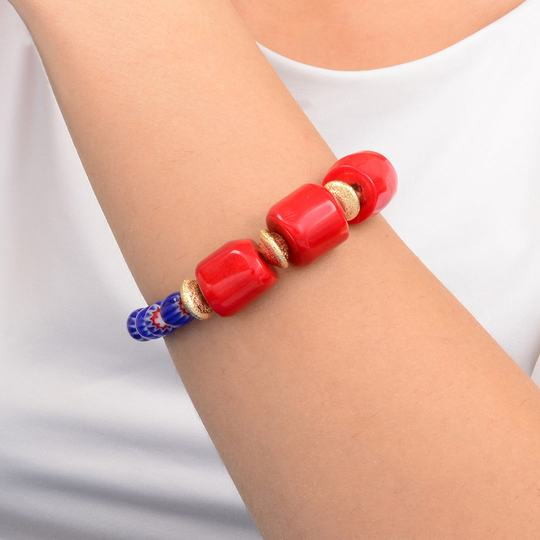 Red beaded bracelet with gold accents on a wrist against a white background
