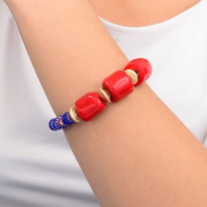 Red beaded bracelet with gold accents on a wrist against a white background
