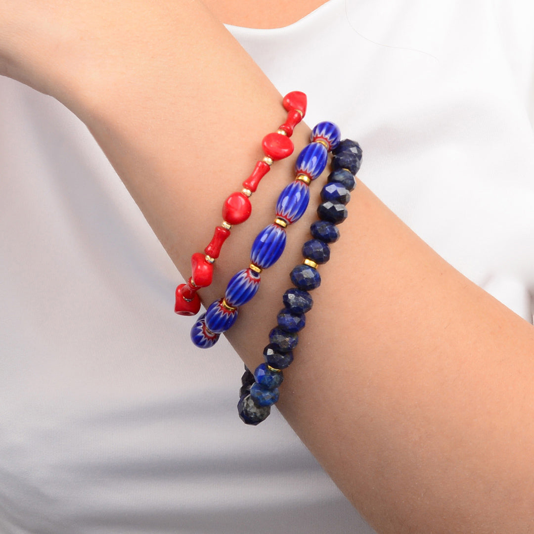 Three beaded bracelets, one red and two blue, on a person's wrist against a white background.