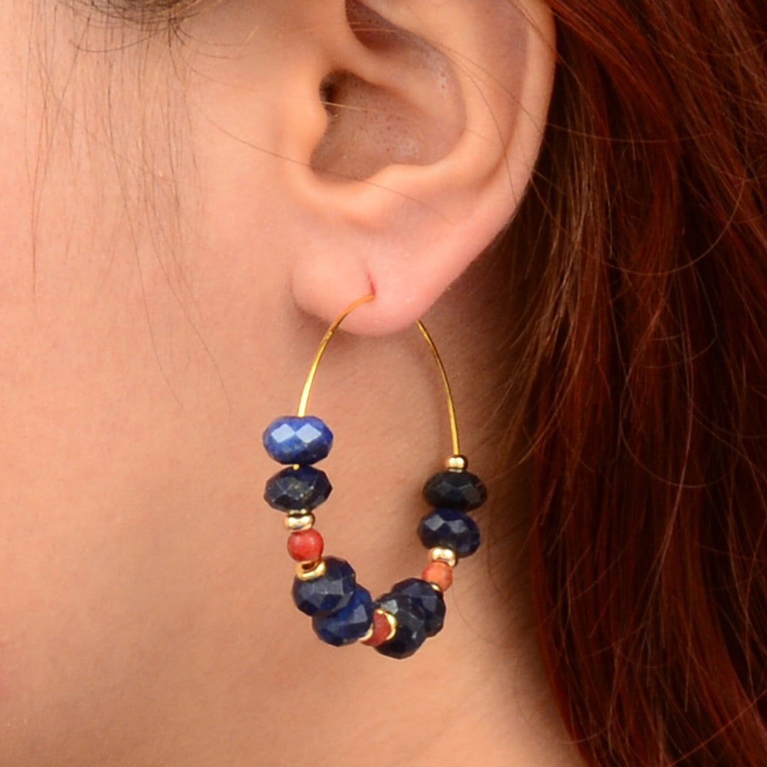 Close-up of an ear wearing a hoop earring with blue and red beads.