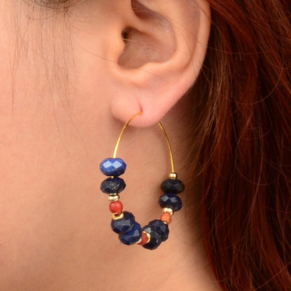 Close-up of an ear wearing a hoop earring with blue and red beads.
