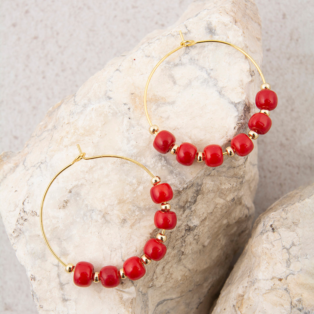 Gold hoop earrings with red beads on a stone surface