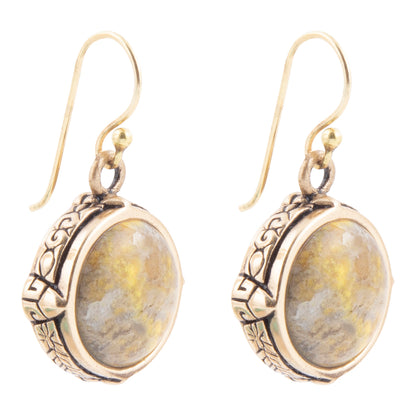 A pair of dangling earrings with oval cabochon stones featuring yellow and gray marbling, set in ornate antiqued gold-tone metal with fishhook wires.