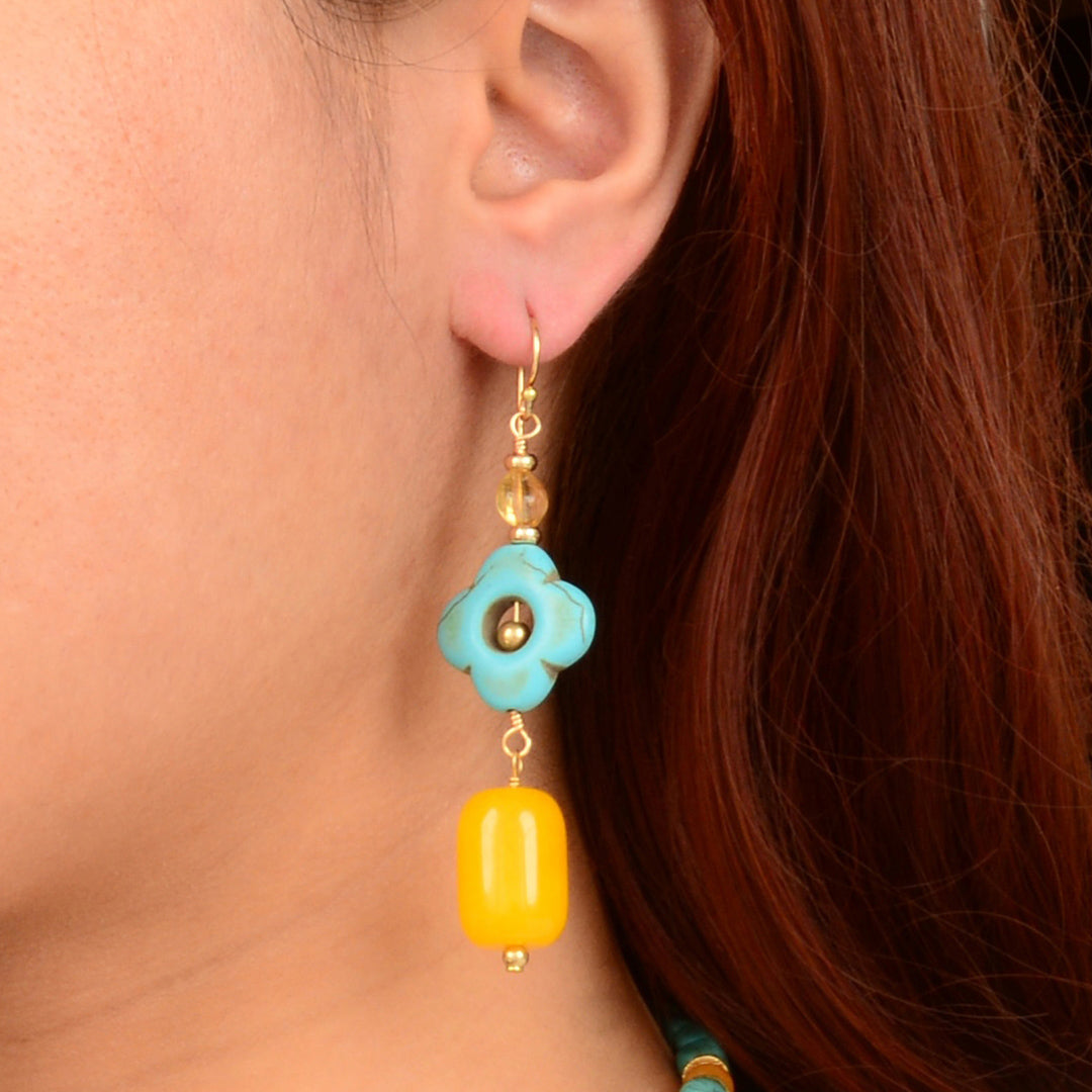 Close-up of a turquoise and yellow earring on an ear with red hair.