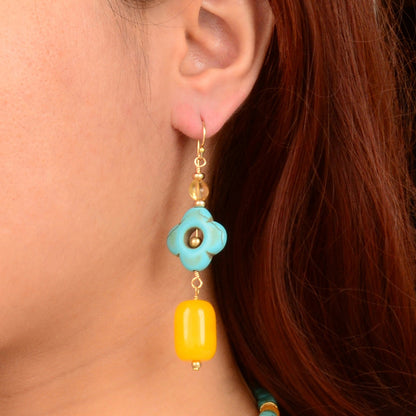 Close-up of a turquoise and yellow earring on an ear with red hair.