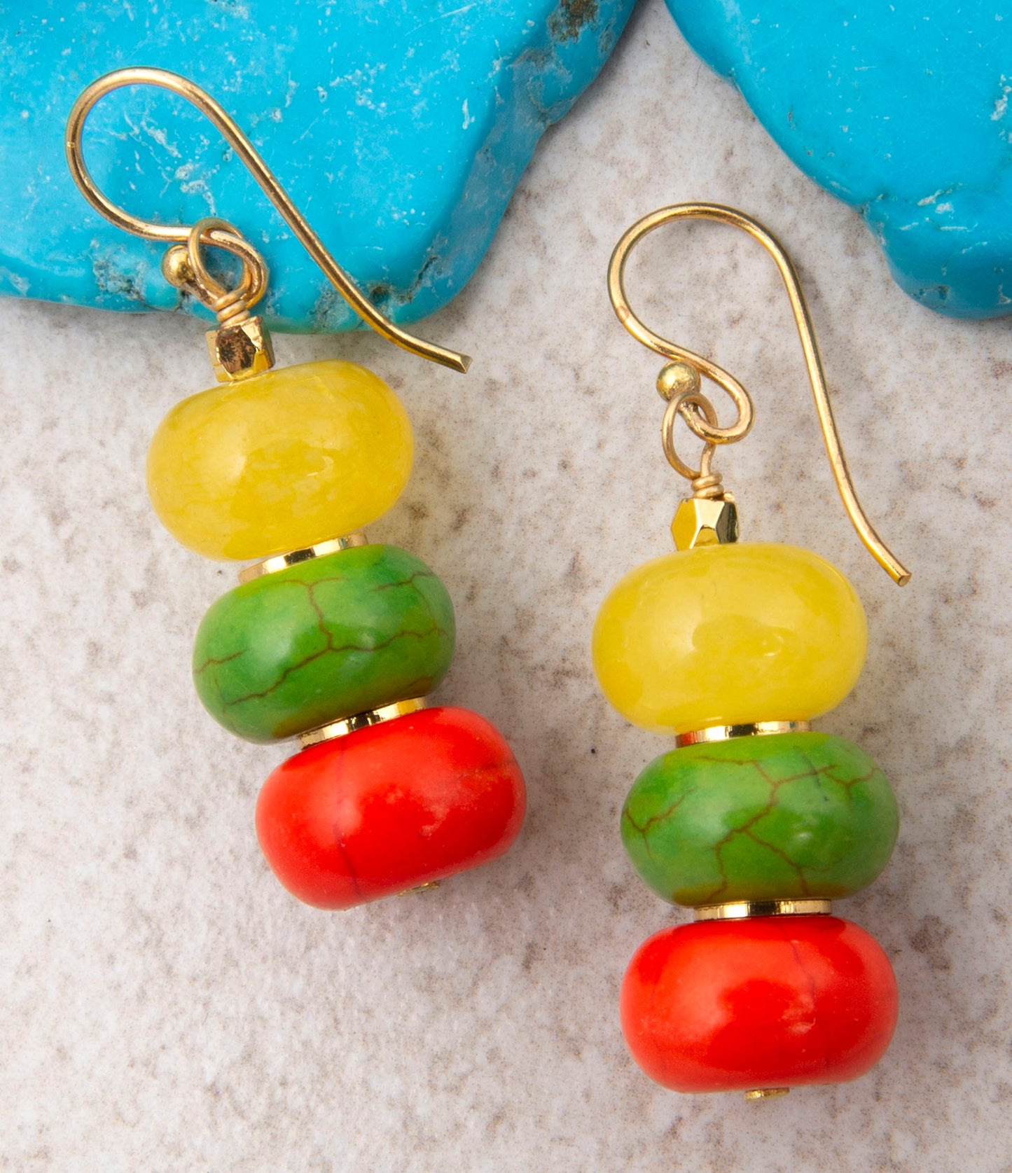 Colorful beaded earrings with gold hooks on a textured surface.