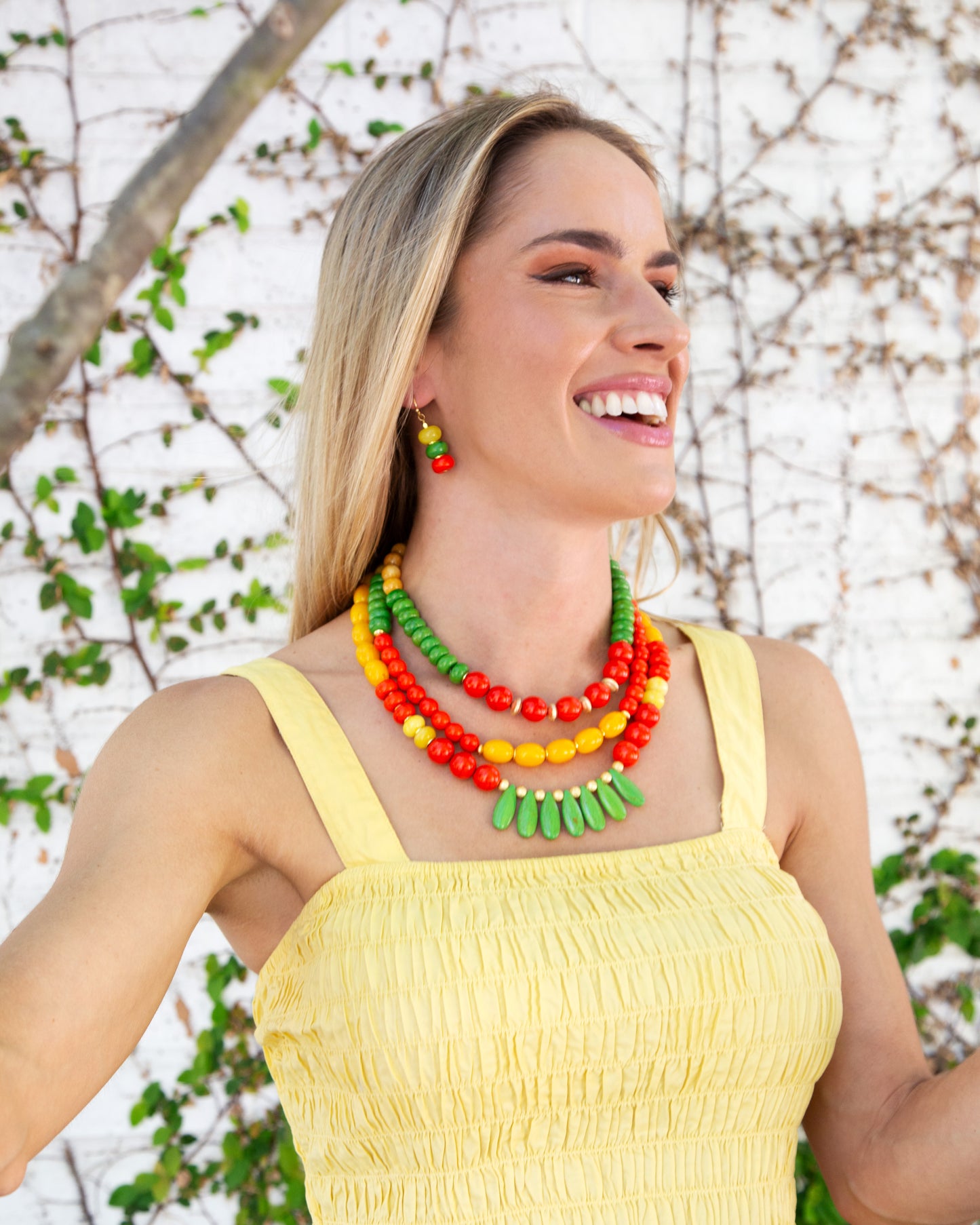 Woman wearing a colorful necklace and yellow top against a natural background