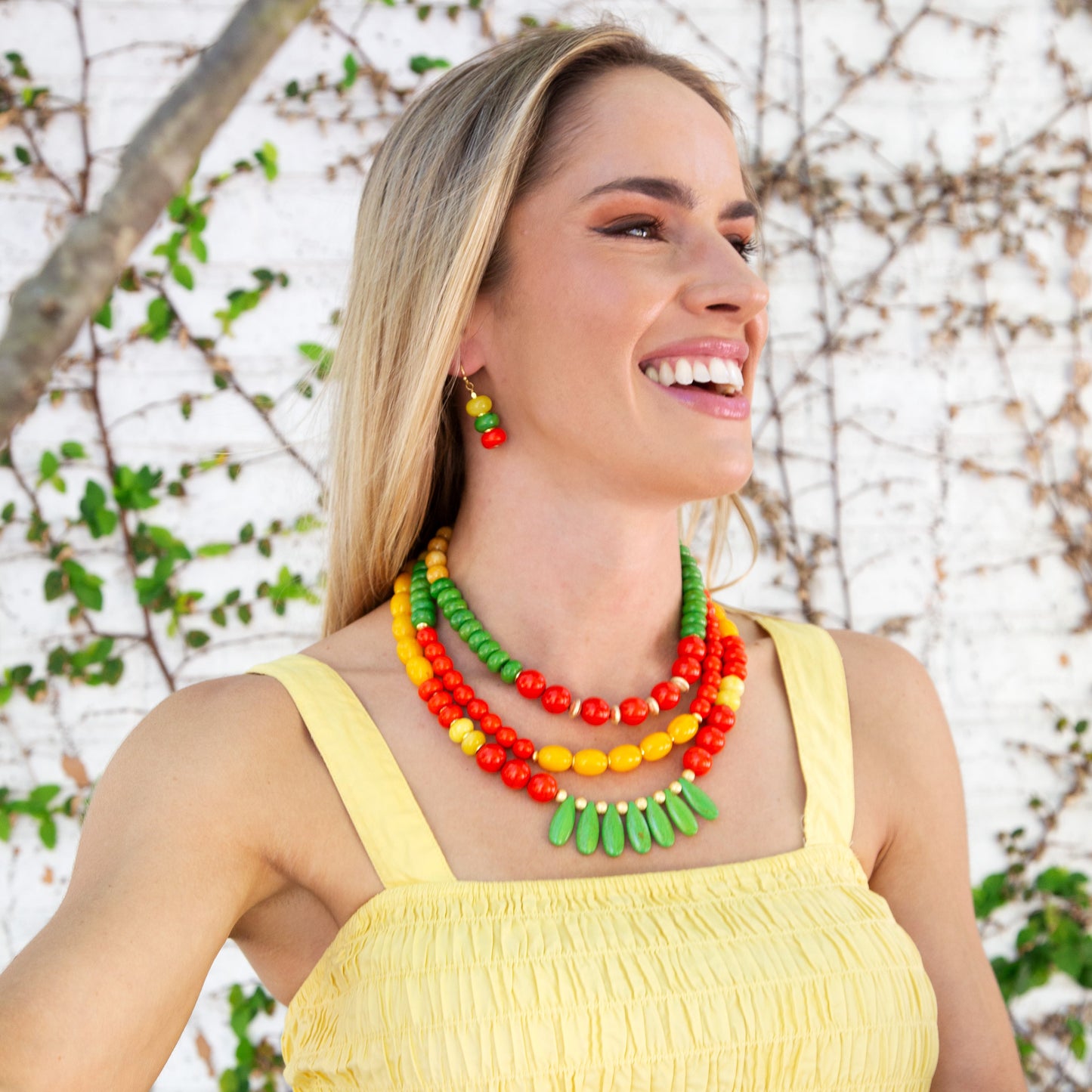 Woman wearing a colorful necklace and yellow top against a natural background