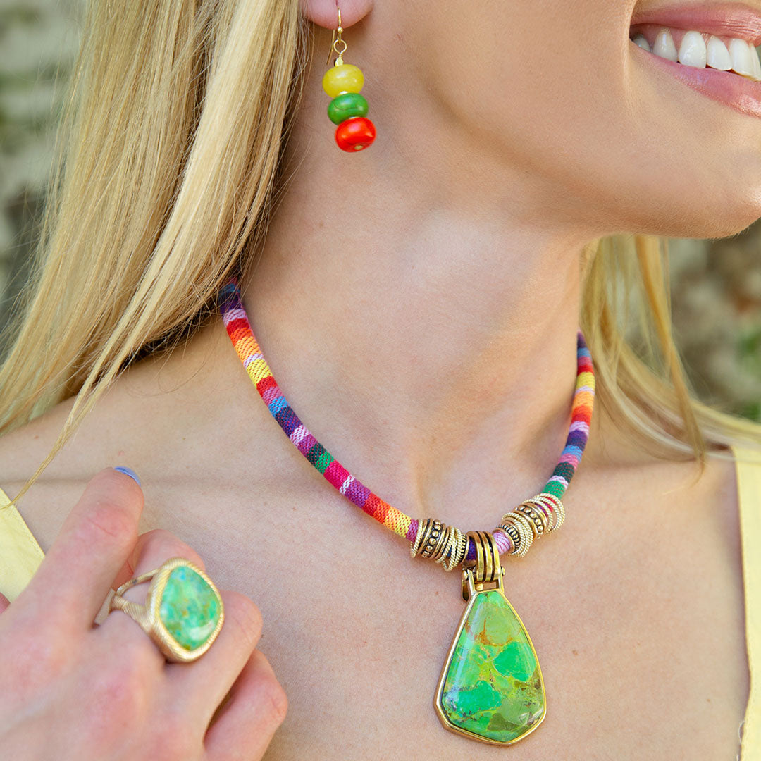 Woman wearing a colorful necklace with a large green pendant and matching earrings.
