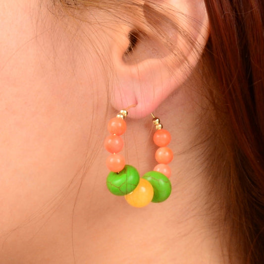 Close-up of a person wearing colorful beaded hoop earrings.