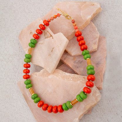 Necklace with green, red, and brown beads on a textured background