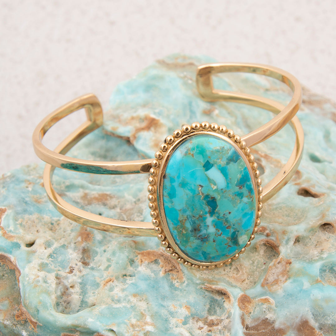 Gold bracelet with a turquoise stone on a textured surface