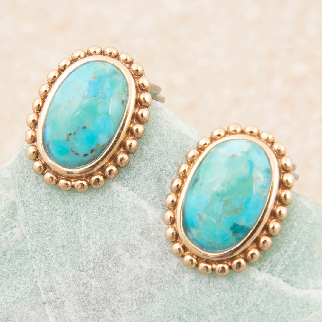 Turquoise stone earrings with gold accents on a light green surface