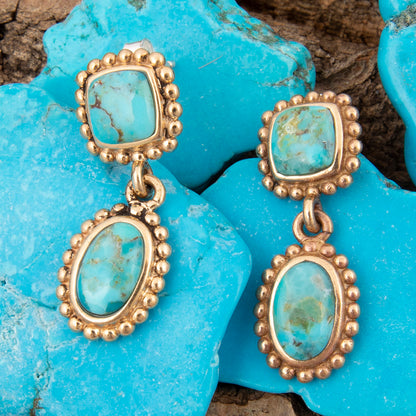 Gold earrings with turquoise stones on a blue stone background