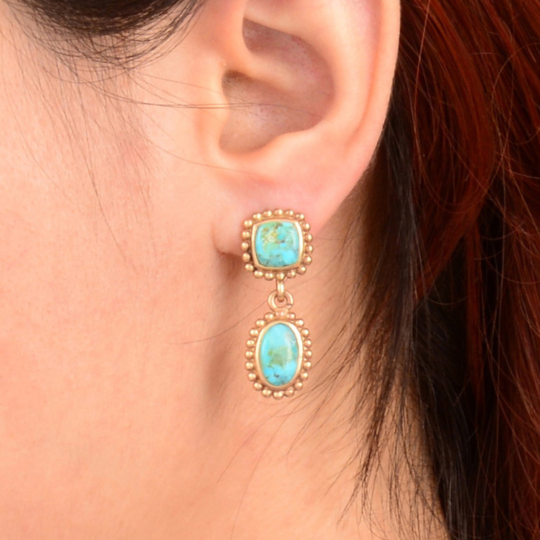 Turquoise earrings with gold accents worn by a person