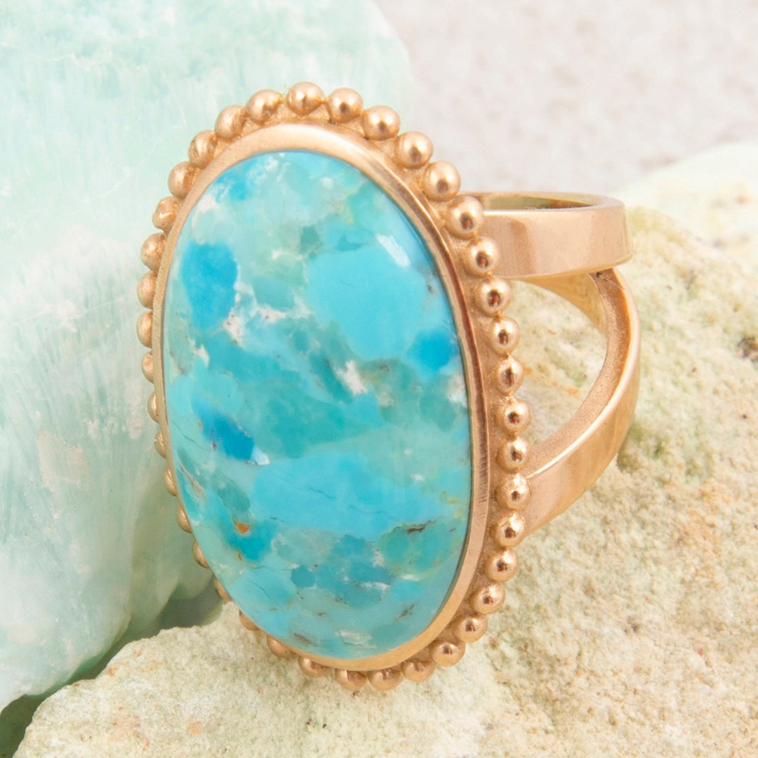 Gold ring with a large turquoise stone on a textured surface