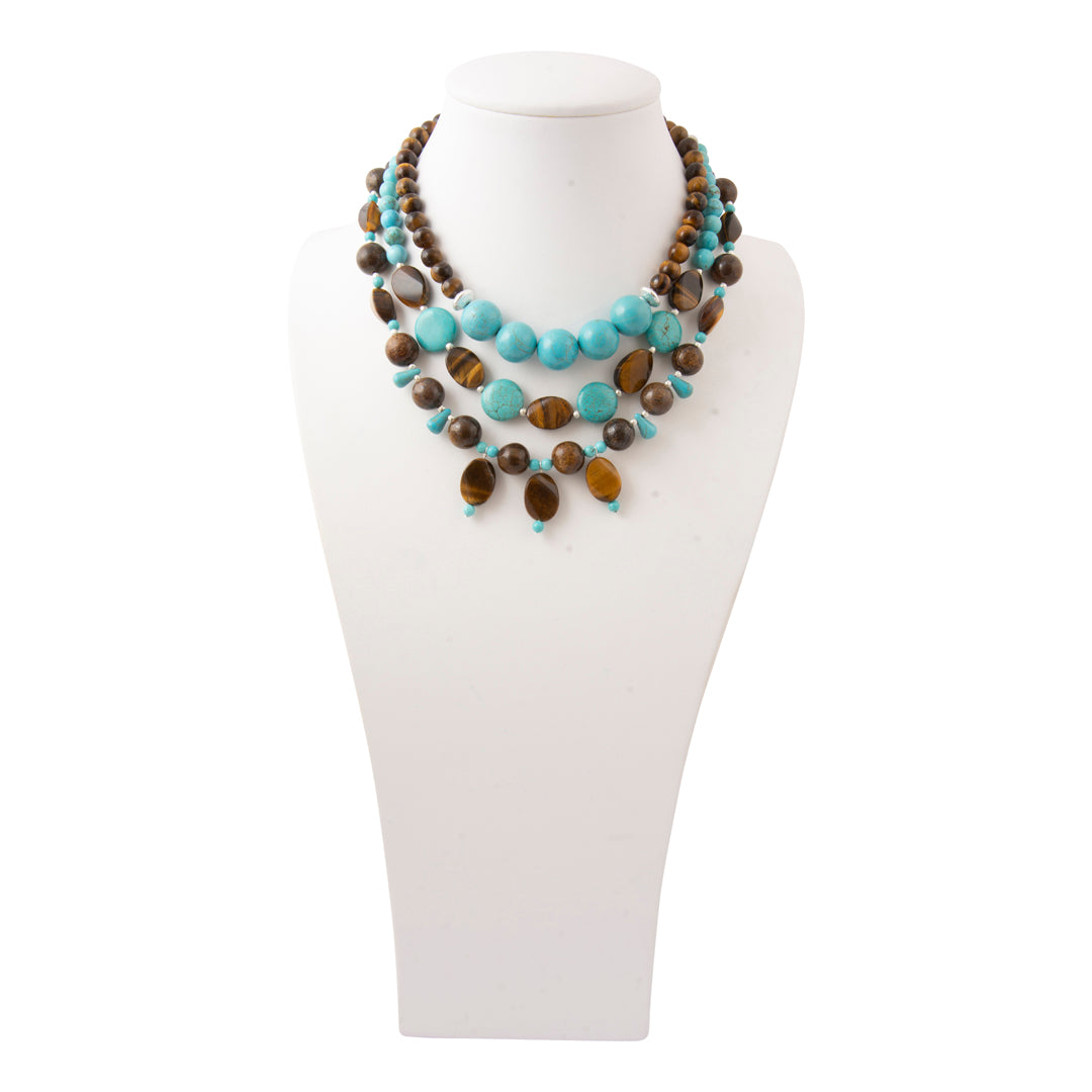 A multi-strand statement necklace featuring turquoise, brown, and tiger's eye beads, displayed on a white mannequin bust against a white background.