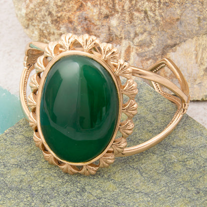 Gold bracelet with a green stone on a stone surface