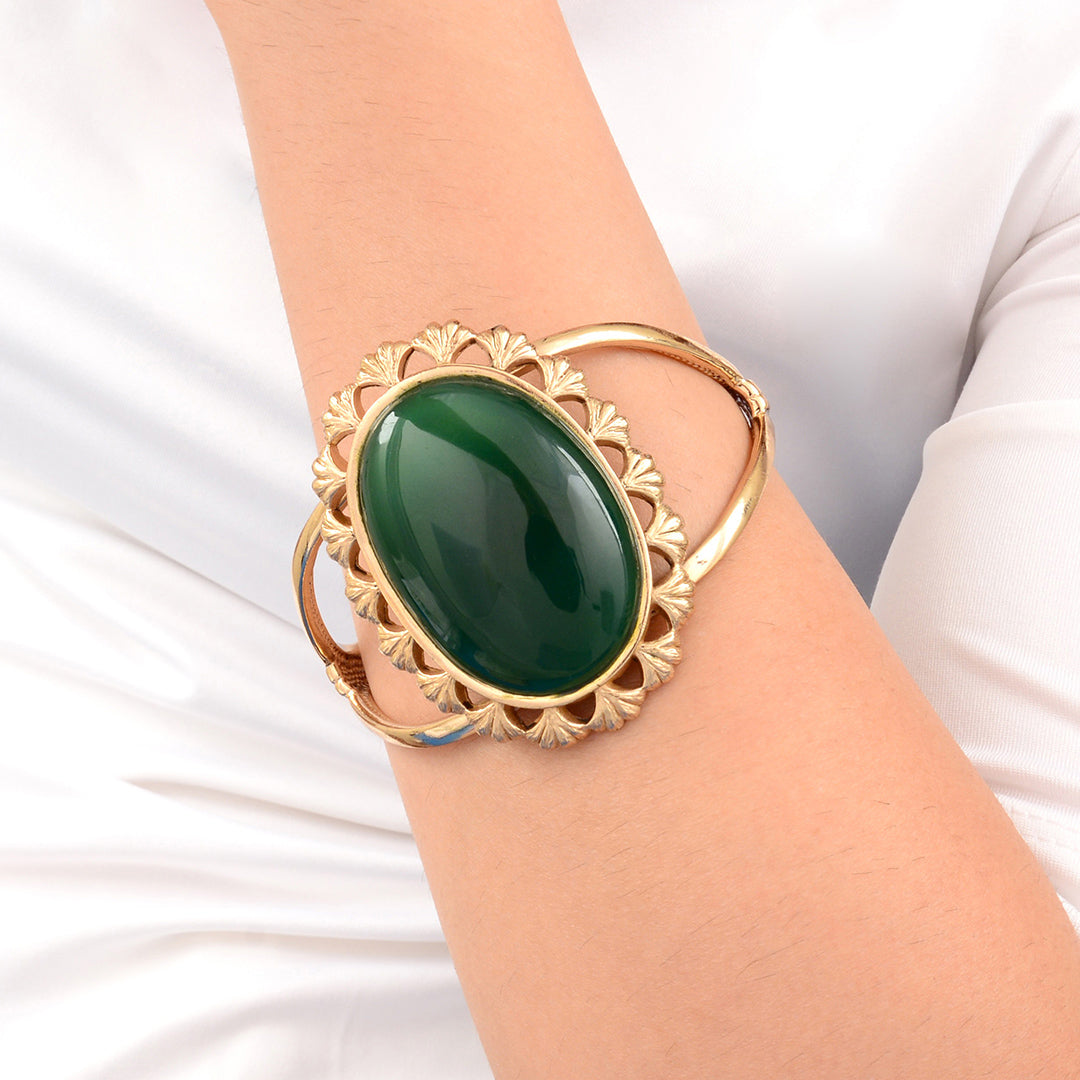 Gold bracelet with a green stone on a white background