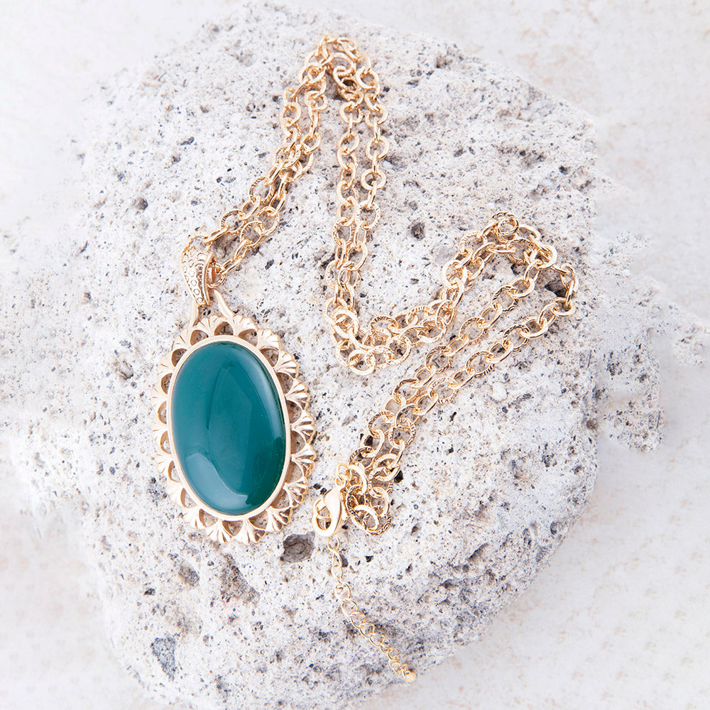 Gold necklace with a green pendant on a textured stone surface