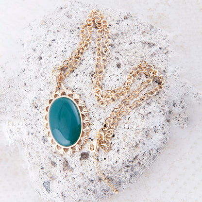 Gold necklace with a green pendant on a textured stone surface
