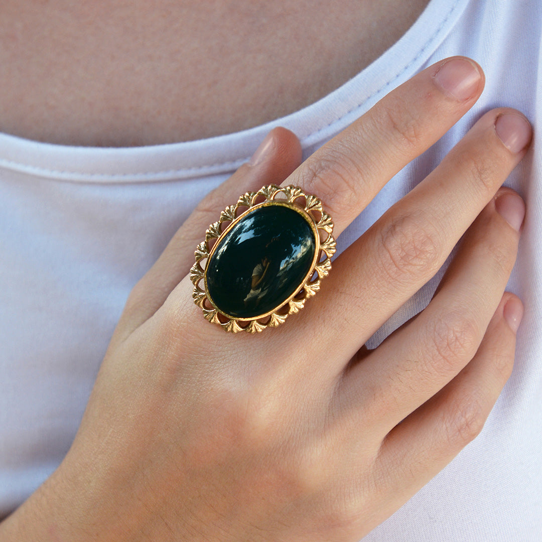 Hand wearing a gold ring with a green stone against a white background