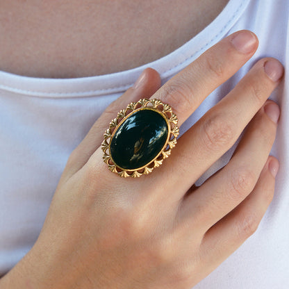 Hand wearing a gold ring with a green stone against a white background