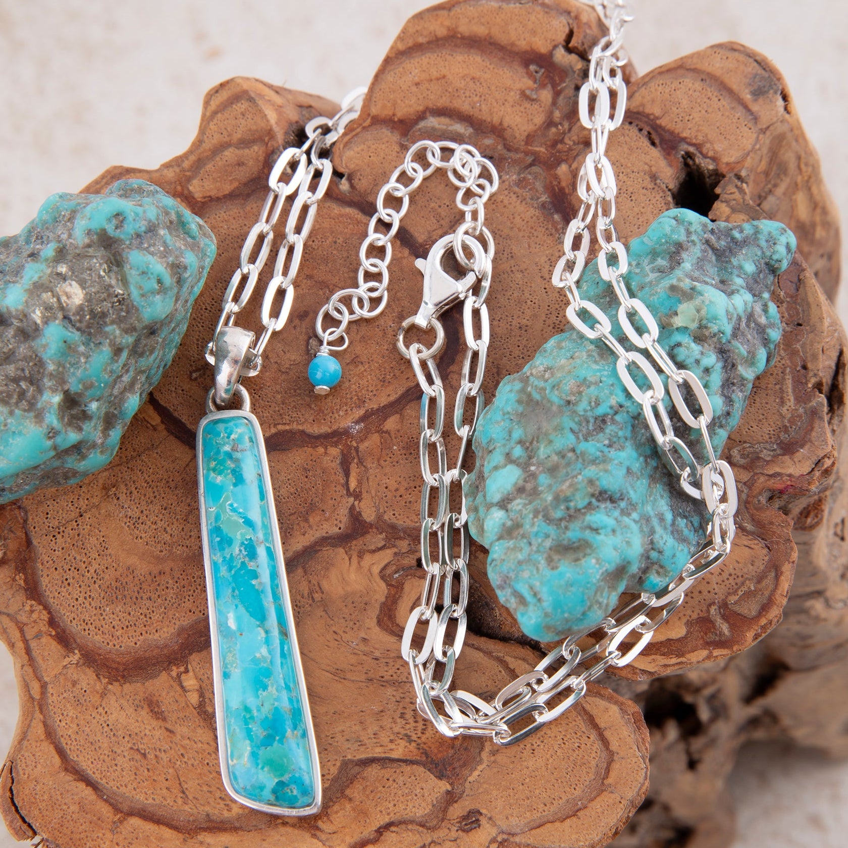 Silver chain necklace with turquoise pendant on a textured stone surface