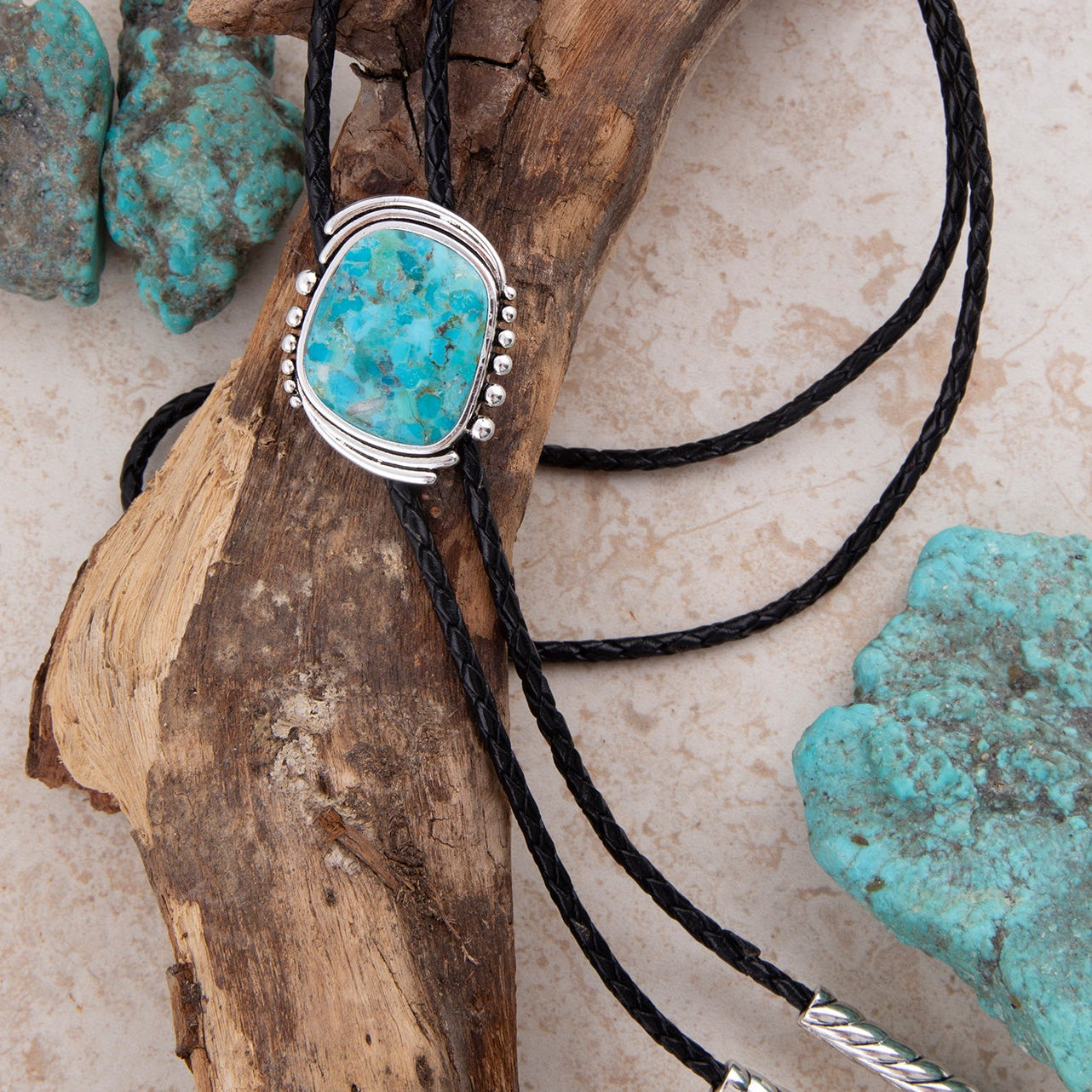 Turquoise stone bolo tie on black cord with turquoise stones in the background