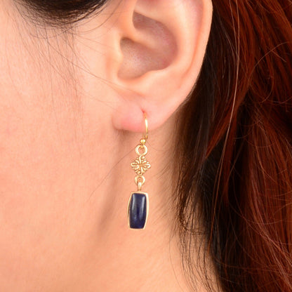 Gold earring with a blue gemstone worn by a person with red hair.