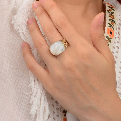 Hand wearing a ring with a large pearl-like stone against a textured fabric background
