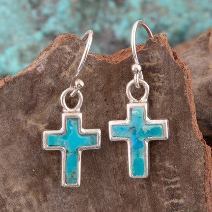 Silver cross earrings with turquoise stones on a stone surface