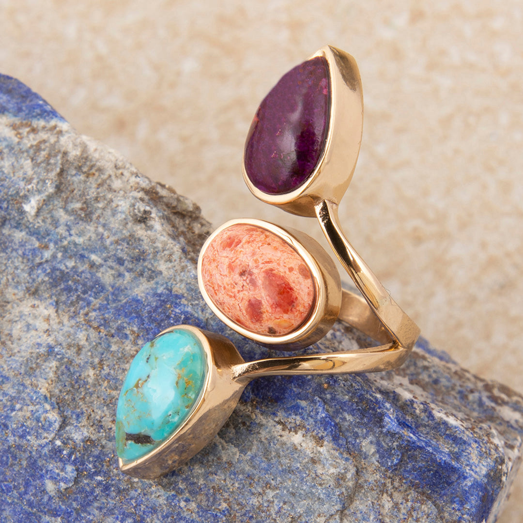 Three gold rings with different colored stones on a stone surface