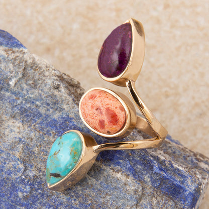Three gold rings with different colored stones on a stone surface