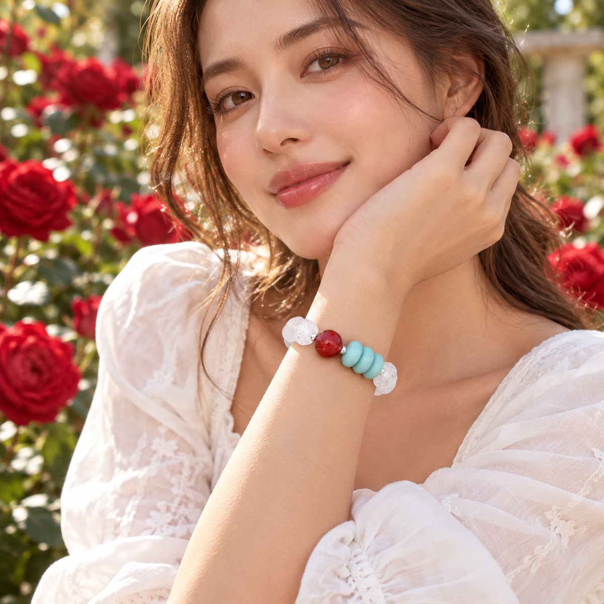 A woman in a white lace top wearing a beaded bracelet with white, light blue, and red beads, posing outdoors in front of a background of red roses.