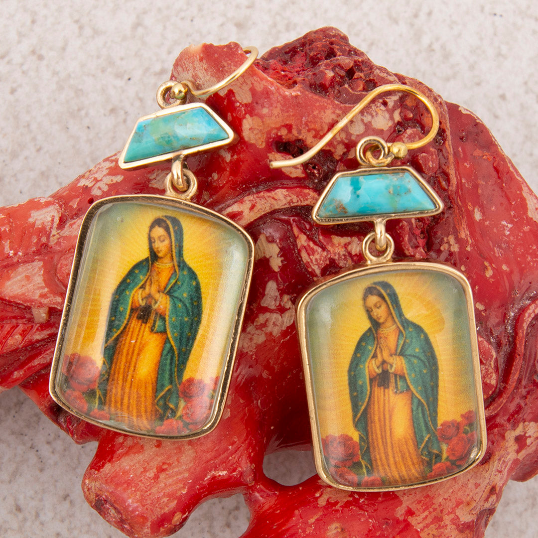 Gold-framed earrings with religious iconography on a textured red stone background