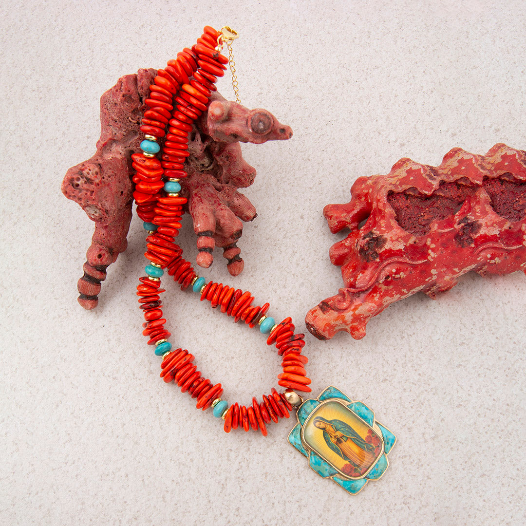 Coral necklace with turquoise beads and a religious pendant on a textured surface