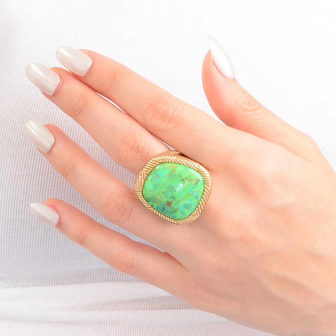 Hand wearing a gold ring with a green stone on a white background