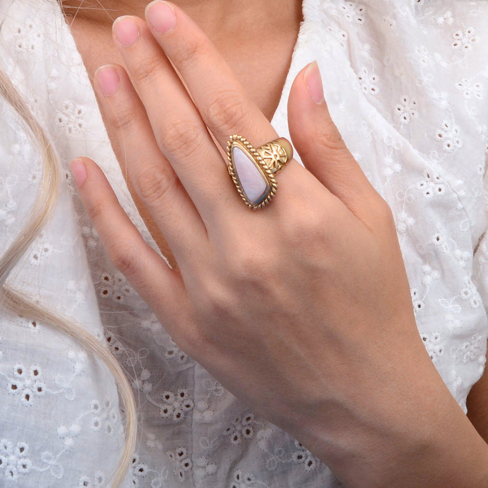Hand wearing a gold ring with a stone on a white lace background