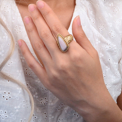 Hand wearing a gold ring with a stone on a white lace background