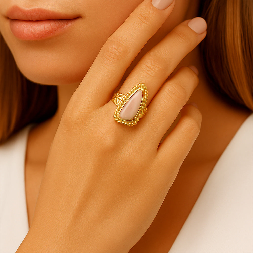 Close-up of a hand wearing a gold ring with a pink stone, against a neutral background.