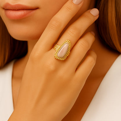 Close-up of a hand wearing a gold ring with a pink stone, against a neutral background.