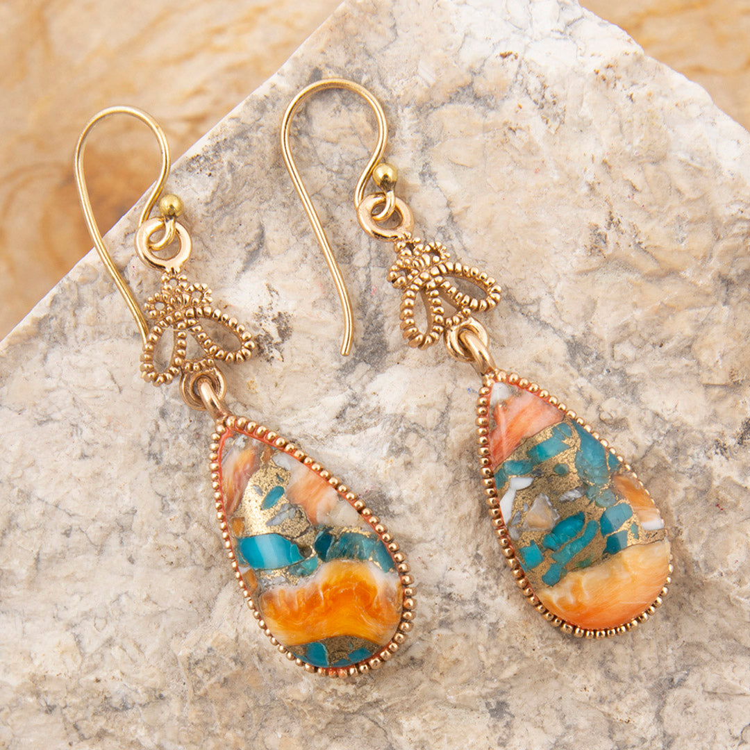 Pair of gold earrings with teardrop-shaped multicolored stones on a marble surface