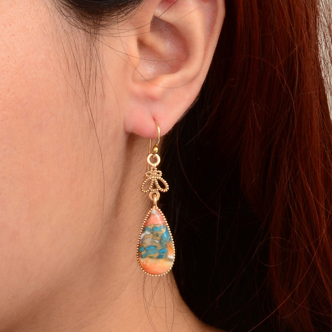 Close-up of a person wearing a teardrop-shaped earring with a colorful stone.
