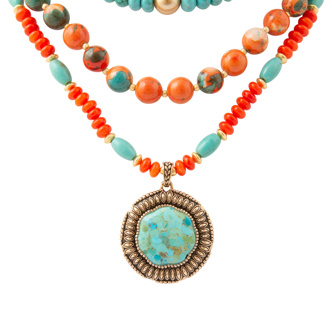 A bohemian-style beaded necklace featuring vibrant orange coral beads, turquoise blue beads, and marbled orange-and-turquoise stone beads, with a large round turquoise pendant in an ornate bronze bezel setting.
