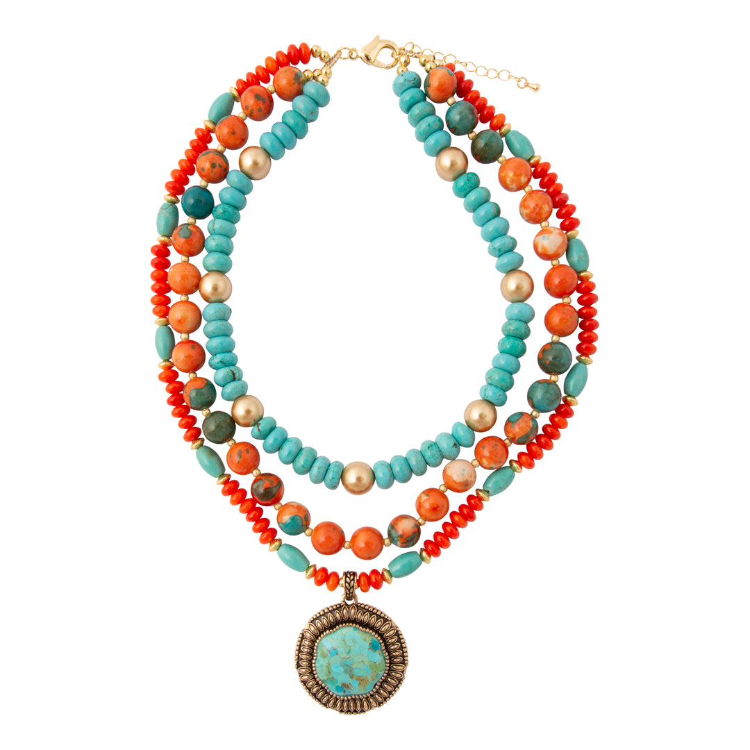 A multi-strand beaded necklace featuring turquoise, orange, and coral beads with a large oval turquoise pendant, displayed on a clean white background.