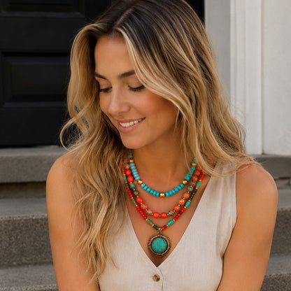 A woman wearing a layered bohemian-style necklace with turquoise, red, and orange beads, sitting on outdoor stone steps.