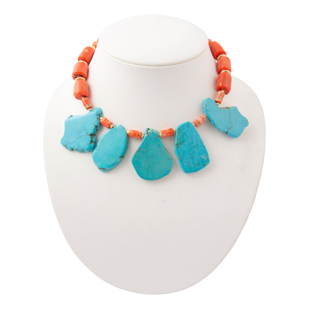 A statement necklace featuring five large, irregular turquoise-blue stone pendants suspended from a strand of coral-orange beads, displayed on a white mannequin bust.
