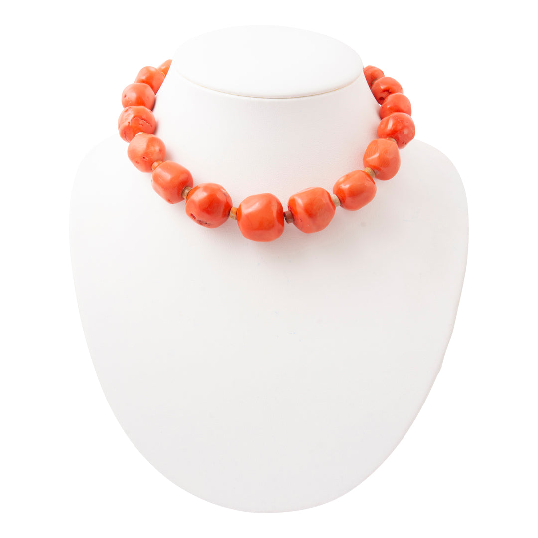 A chunky coral-orange beaded necklace displayed on a white jewelry bust against a white background.